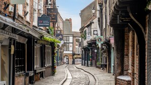 Una estrecha calle empedrada flanqueada por edificios tradicionales, algunos con letreros de negocios como una sala de té y una joyería.