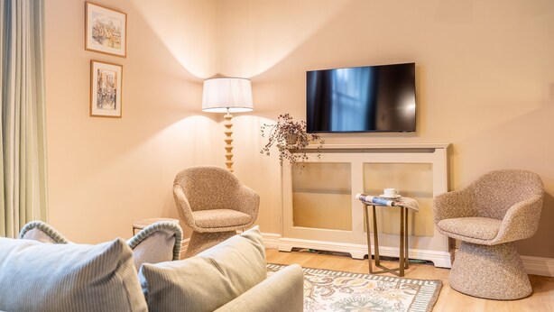 Una sala de estar acogedora con un sofá, dos sillones, un televisor sobre la chimenea y una mesita con una lámpara.