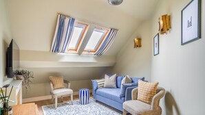 A cozy living room with a blue sofa, two armchairs, a patterned rug, and a ceiling skylight. - The Shambles – The Timbered Nest - A premium stay that sleeps 4 guests (York)