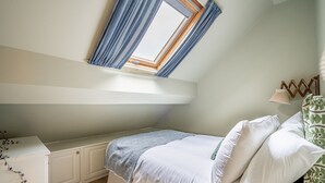 A bedroom with a skylight, a bed with white bedding, a bedside table, and a patterned wall hanging. - The Shambles – The Timbered Nest - A premium stay that sleeps 4 guests (York)