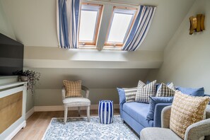 Una sala acogedora con un sofá azul, un sillón blanco y un tapete estampado.