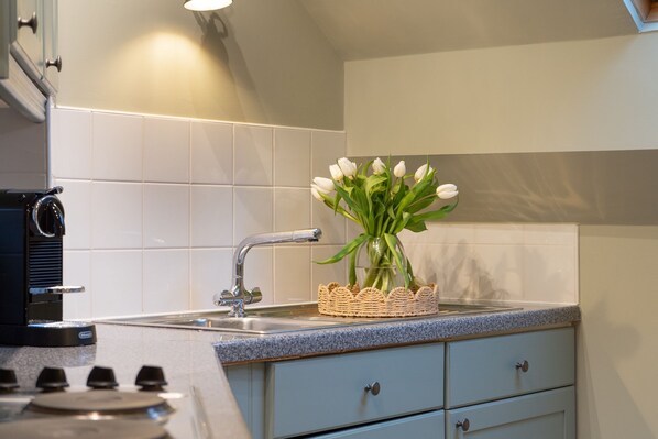 A modern kitchen with a gas stove, a sink, and a vase of white tulips on the countertop. - The Shambles – The Timbered Nest - A premium stay that sleeps 4 guests (York)