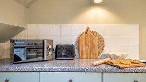 A kitchen with a built-in Russell Hobbs microwave, a toaster, a wooden cutting board, and a bowl of cookies on the counter. - The Shambles – The Timbered Nest - A premium stay that sleeps 4 guests (York)