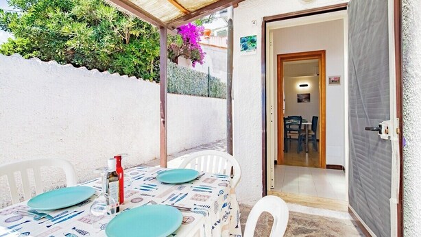 A patio with a table set for two, a door leading to an interior room, and a covered area with plants.