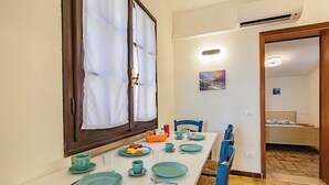A dining area with a white table set for four, blue chairs, and a window with curtains.
