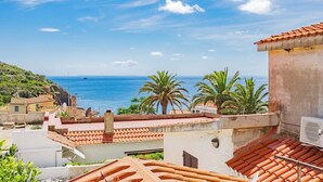 A coastal view with terracotta-tiled buildings, palm trees, and a clear blue sky.