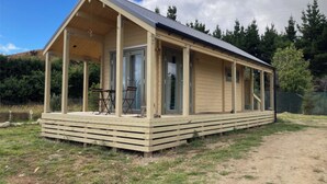 En envåningsstuga i trä med en inglasad veranda, stora skjutbara glasdörrar och ett litet bord med tillhörande stolar utomhus.