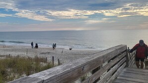 Una playa con un paseo marítimo de madera que conduce a la orilla, gente caminando y un perro en la playa.