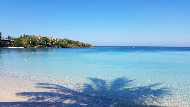 Una playa despejada con aguas tranquilas, una orilla arenosa y una pequeña isla con edificios al fondo.