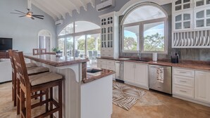 Cozinha espaçosa com armários brancos, uma ilha grande com banquetas e vista para o exterior através de amplas janelas.
