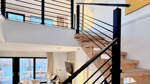 Ein modernes Interieur mit einer Treppe, die zwei Ebenen verbindet, einem Wohnbereich mit Sofa und Couchtisch sowie einem großen Fenster mit Blick ins Freie.