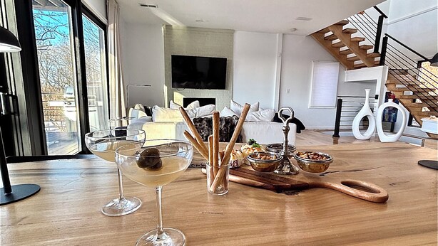 Ein modernes Wohnzimmer mit einem Holztisch, gedeckt für eine Mahlzeit, einem Fernseher und einer Treppe.