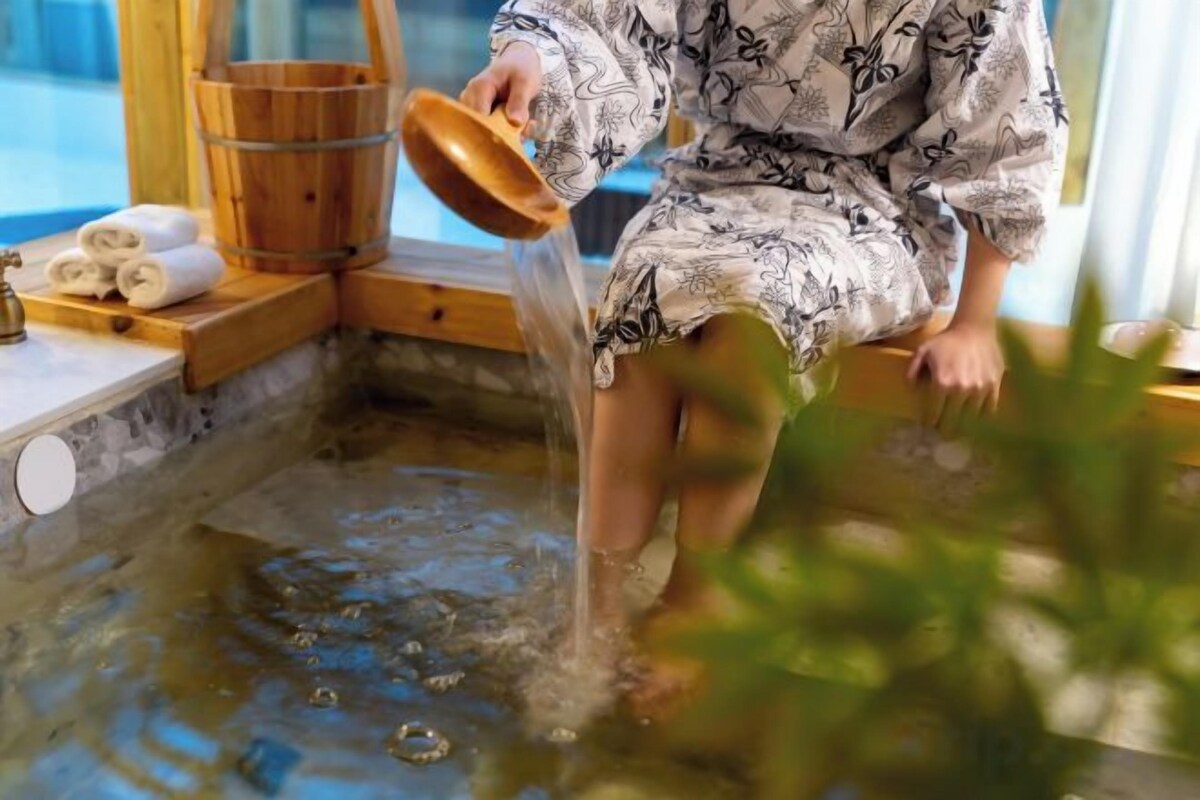 Une personne en peignoir qui verse de l’eau dans une source thermale.