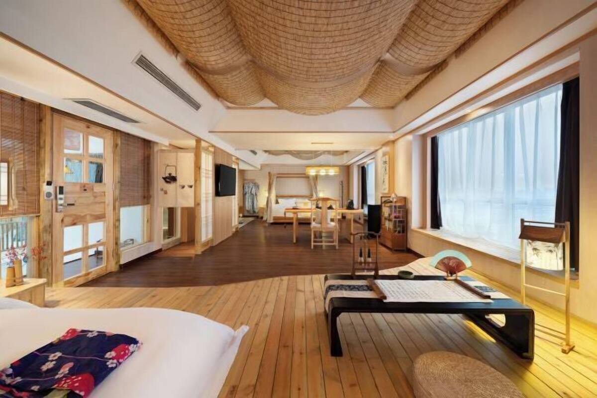 Ein modernes Hotelzimmer mit einem großen Bett, Holzboden, einer Essecke und einem großen Fenster.