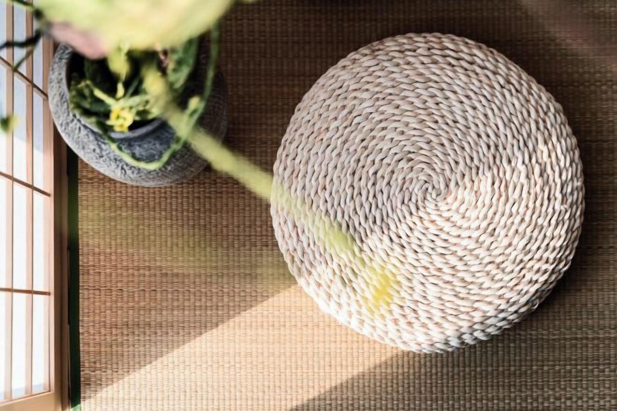A woven basket on a textured mat, a potted plant, and a window with vertical blinds.