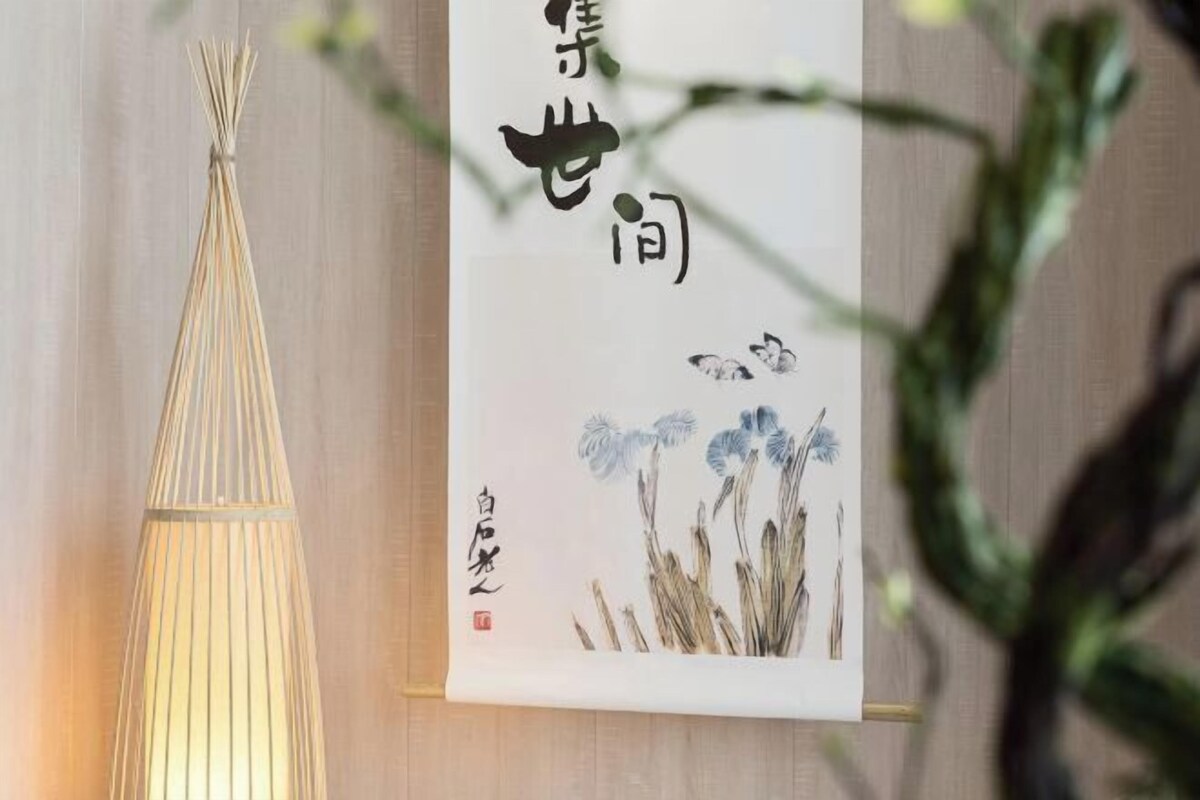A room with a hanging scroll, a conical light fixture, and a plant.