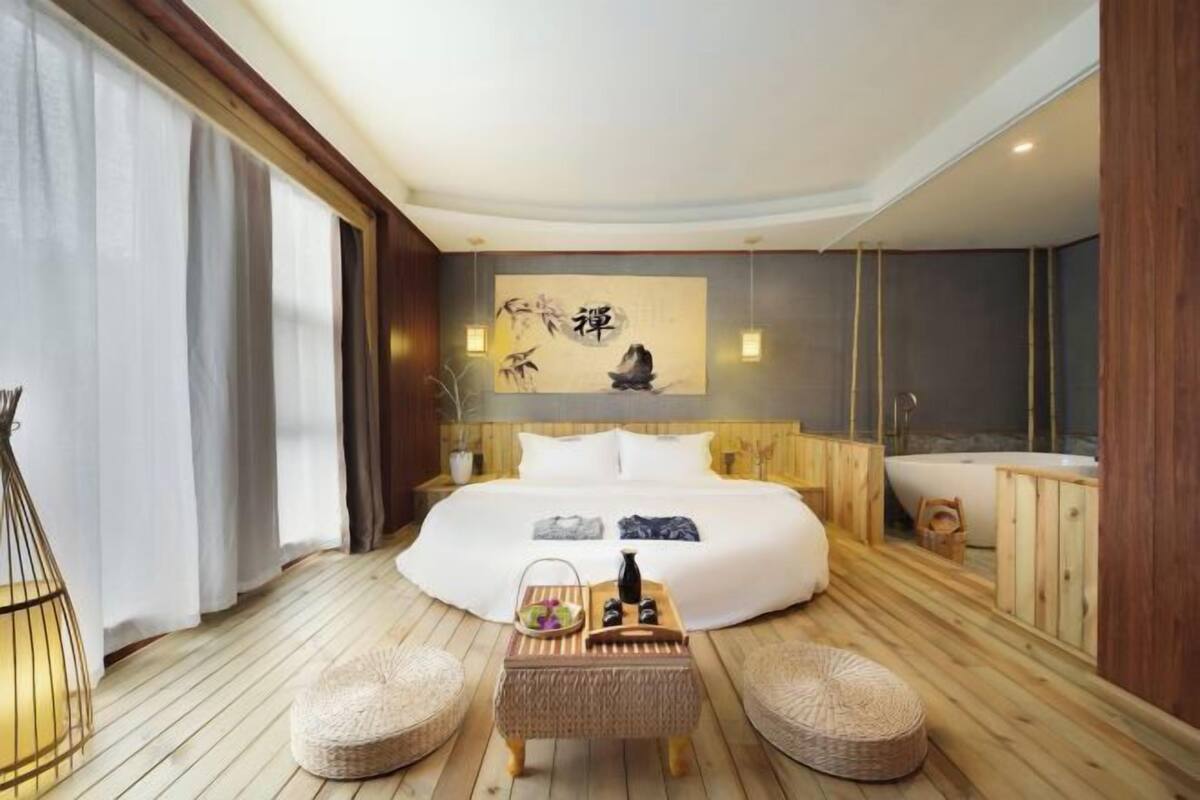 Ein Zimmer mit einem großen Bett, Holzboden, einem Wandbild, einem kleinen Tisch mit Gegenständen und einer Badewanne.