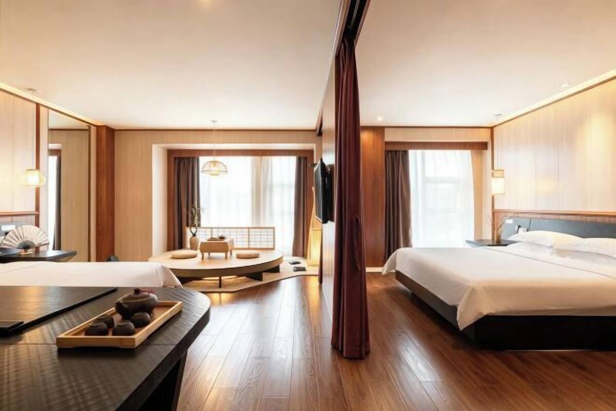 Ein Hotelzimmer mit zwei Betten, einer Sitzecke mit Tisch und Stühlen, einem großen Spiegel und einem Fernseher.