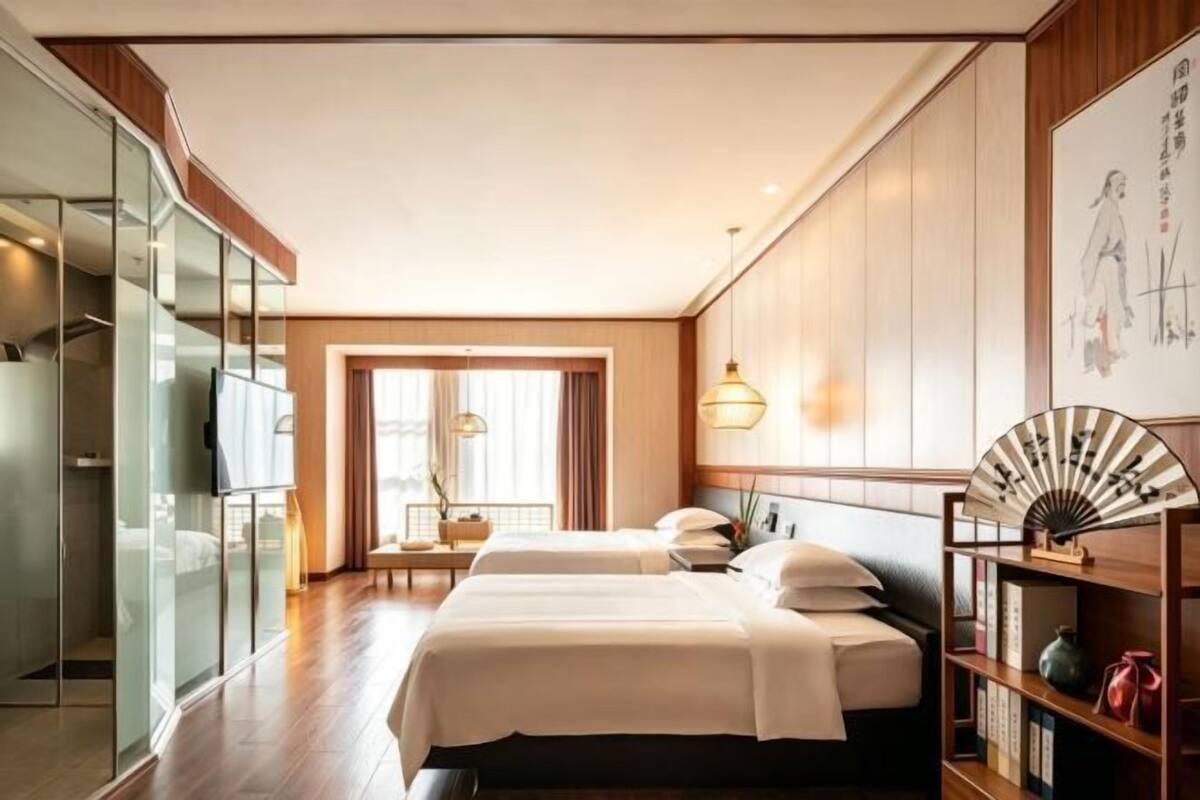 Una habitación de hotel con una cama grande, una mesita de noche, un armario y una ventana con cortinas.