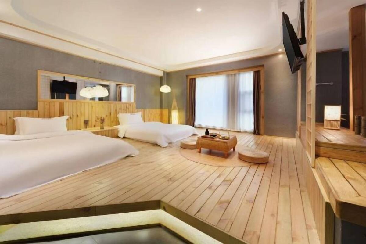 Ein Hotelzimmer mit zwei Betten, Holzboden, einer kleinen Sitzecke, einem Fernseher und einem großen Fenster.