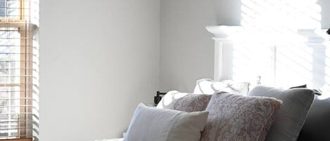 A bedroom with a bed, pillows, a blanket, a framed picture on the wall, and a window with blinds.