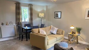 A living room with a beige sofa, a dining table, a lamp, and a radiator. - Idyllic Cottage Sleeps 4 pet Friendly (Appleby-in-Westmorland)