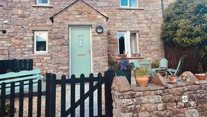 A stone house with a light green door, a small porch with a chair, and a black picket fence. - Idyllic Cottage Sleeps 4 pet Friendly (Appleby-in-Westmorland)
