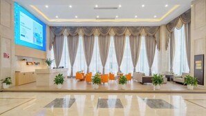 A spacious lobby with a reception desk, seating area, and large windows with curtains.