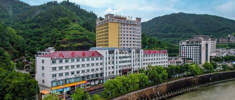 Un hotel de varios pisos con techo rojo, ubicado junto a un río con una represa, rodeado de vegetación y colinas.