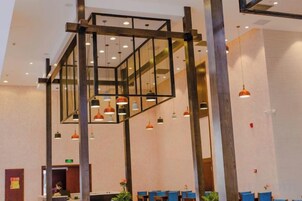 A hotel lobby with a modern design, featuring a central glass partition, multiple hanging pendant lights, and a reception desk.