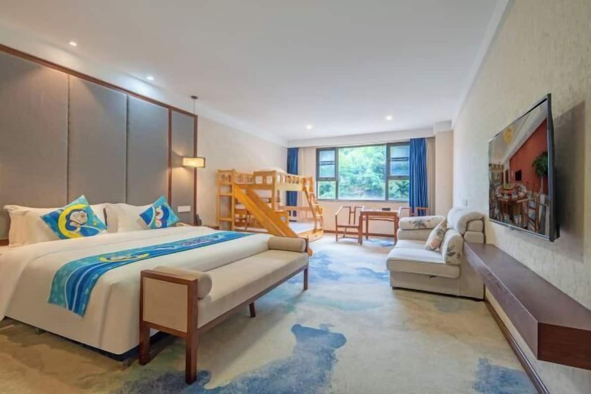 Una habitación de hotel con cama, sofá, escritorio, literas y un ventanal grande.