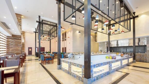 A modern hotel lobby with a central island counter, seating areas, and a staircase.