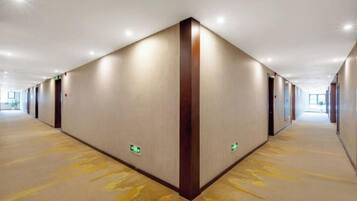 Un largo y estrecho pasillo de hotel con piso alfombrado, paredes con detalles verticales de madera y letreros de salida de emergencia.