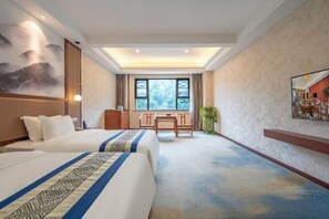 Habitación de hotel con dos camas, un escritorio, una silla, un ventanal grande y un cuadro en la pared.