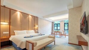 A hotel room with a bed, bedside table, bench, and a view of the outdoors.