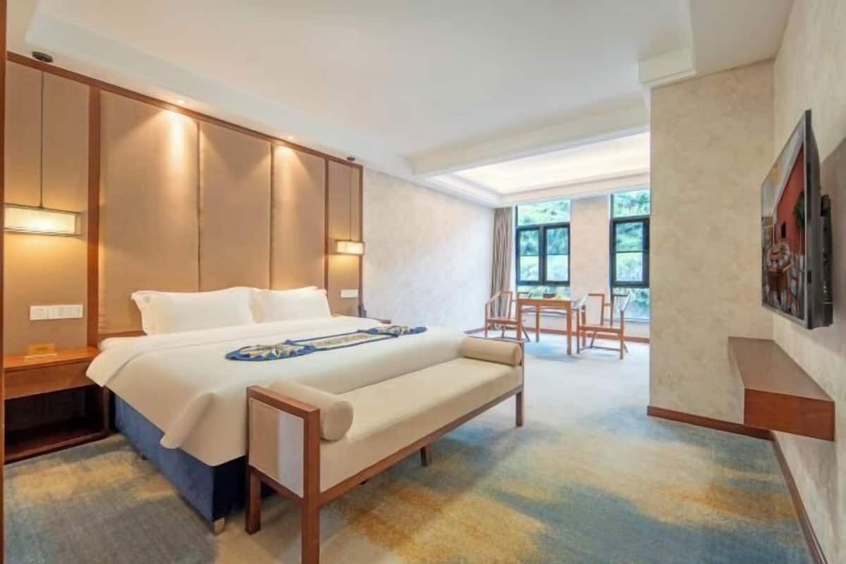 Una habitación de hotel con cama, mesita de noche, banco y vistas al exterior.
