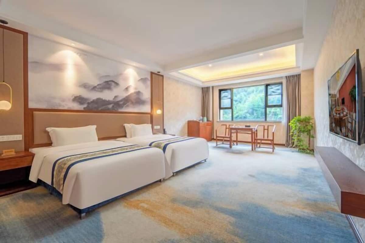 Una habitación de hotel con dos camas, una mesa de comedor y un ventanal grande.