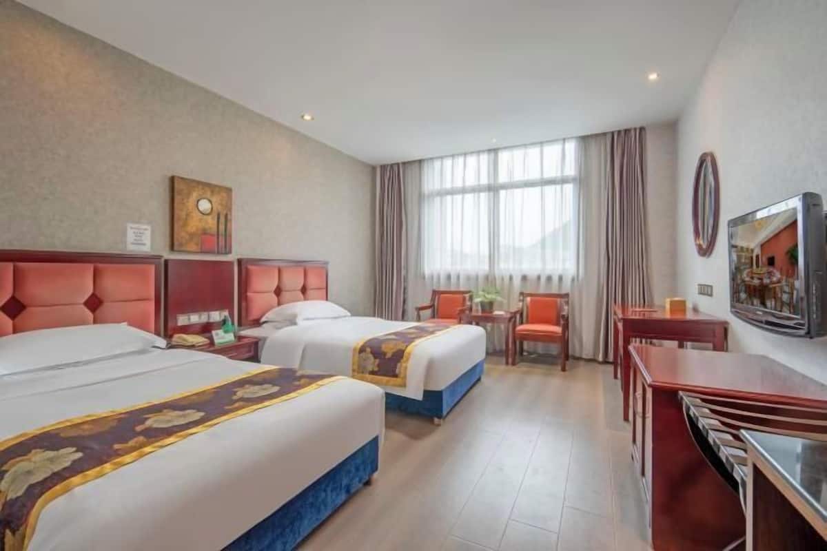 Habitación de hotel con dos camas, un escritorio, una silla, un televisor y una ventana con cortinas.
