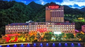 A multi-story hotel with a prominent red sign on the top, surrounded by lush greenery and hills.