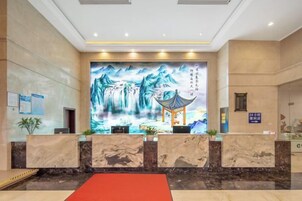 A hotel reception area with a large mural, reception desk, and a red carpet.