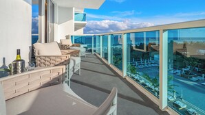 A balcony with a view of the ocean, furnished with chairs and a table, and a bottle of wine.