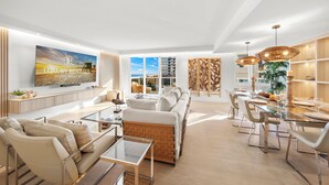 A spacious living room with a large TV, comfortable seating, a dining area with a glass table, and a view of the city.