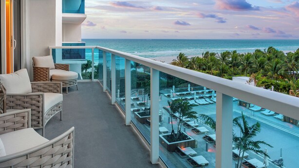 A balcony with a view of the ocean, lounge chairs, and a pool area.