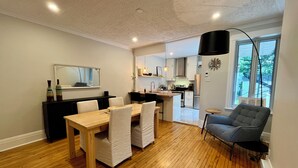 A modern kitchen with white cabinets, a wooden dining table, and a gray sofa. - Montréal Haven (Montréal)