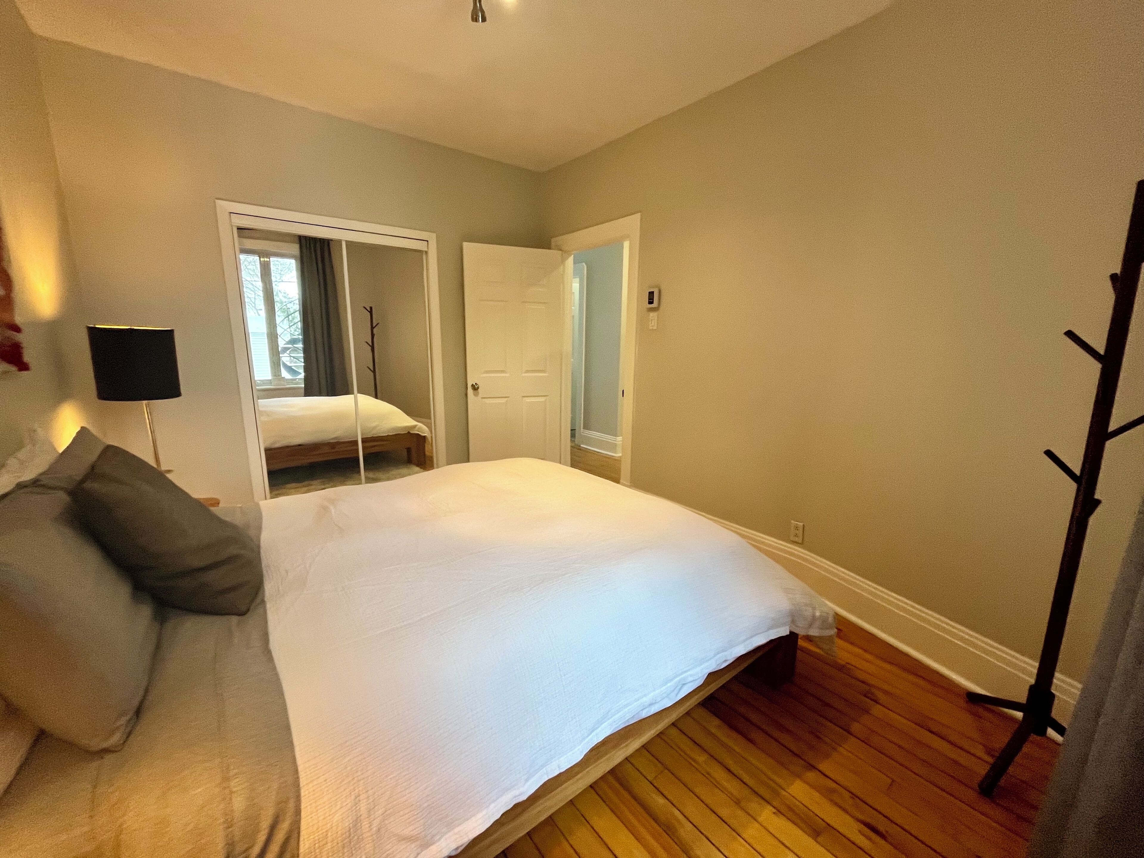 Ein Schlafzimmer mit Bett, Nachttisch, Lampe, Kleiderständer und Kleiderschrank.