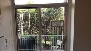 A sliding glass door leading to an outdoor patio area with a view of trees and a wooden fence. - Montréal Haven (Montréal)
