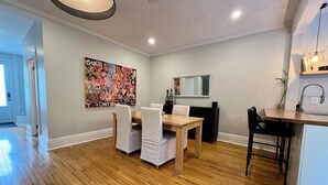 A modern living room with a wooden dining table, white chairs, a large abstract painting, a TV, and a kitchen area with a sink and countertop. - Montréal Haven (Montréal)