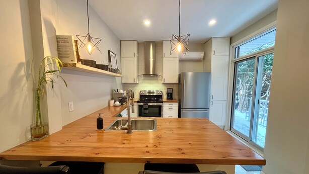 A modern kitchen with a wooden island, stainless steel appliances, and pendant lighting. - Montréal Haven (Montréal)