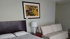 A hotel room with a large bed, a sofa, a nightstand with a lamp, and a ceiling fan. - OCEAN VIEW Studio@Daytona Zzz 4 (Daytona Beach)
