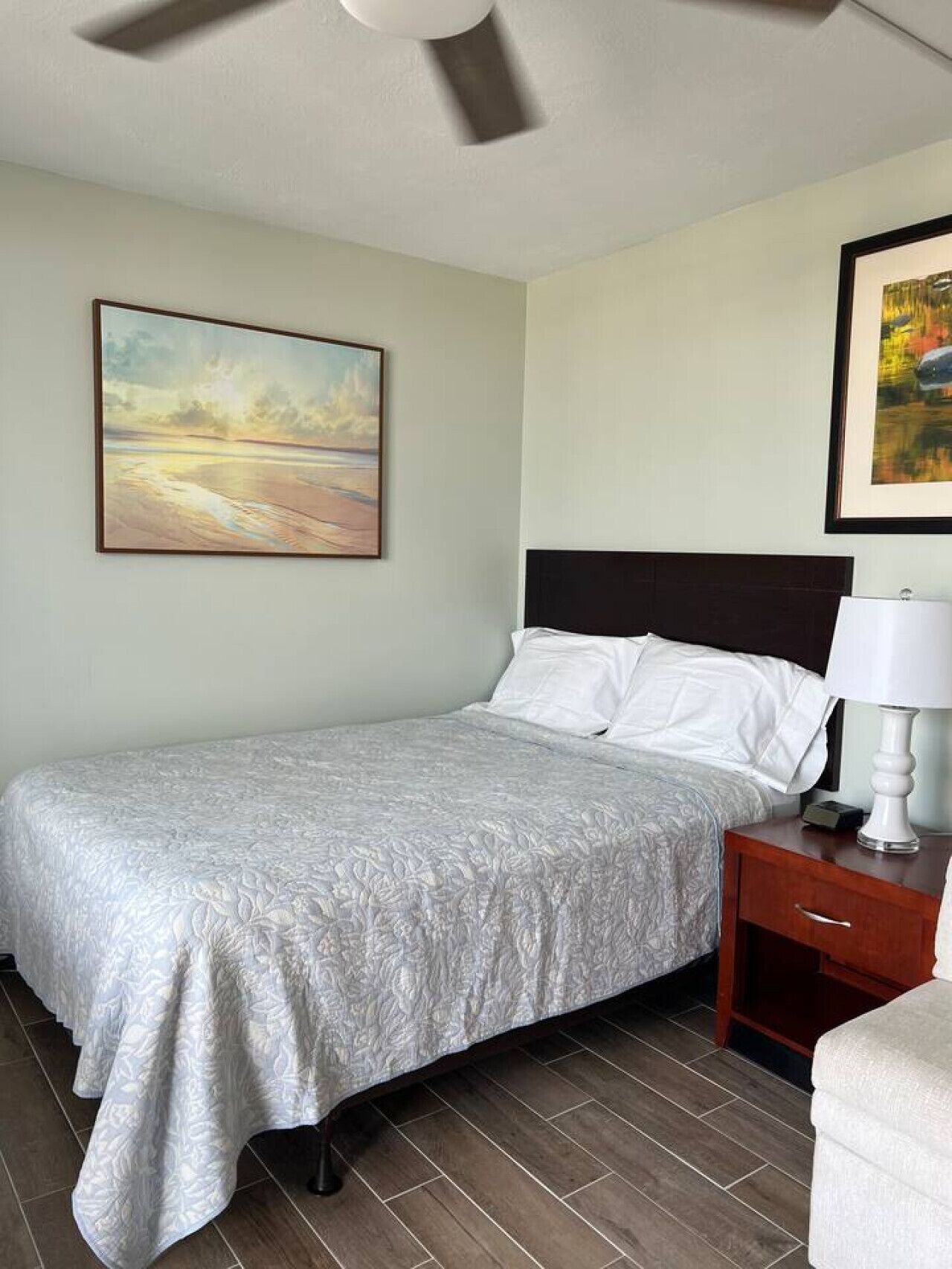 A hotel room with a bed, a nightstand, a lamp, and two framed pictures on the wall.